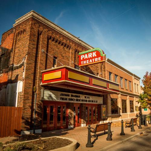 Historic Park Theatre building with a marquee, surrounded by trees and a clear blue sky.