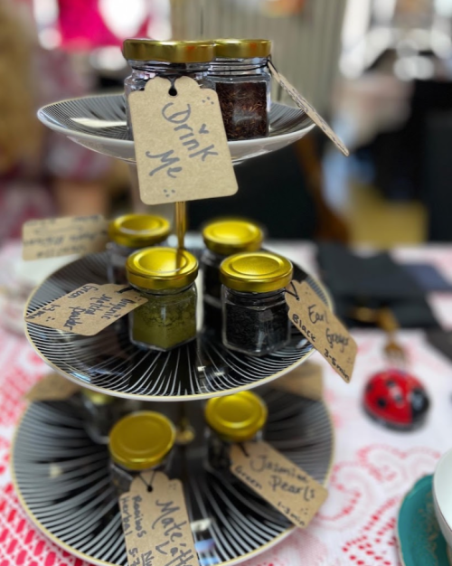A tiered stand with jars of various spreads, each labeled with handwritten tags, inviting guests to "Drink Me."