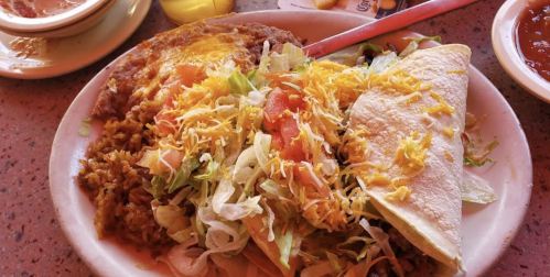A plate of Mexican food featuring a taco, rice, beans, lettuce, tomatoes, and cheese, with salsa on the side.