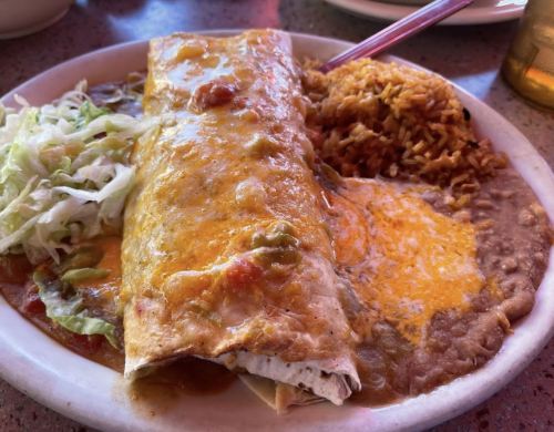 A plate of enchiladas topped with sauce and cheese, served with rice, refried beans, and a side of lettuce.