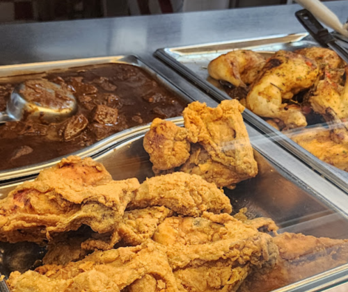 A display of fried chicken and a savory meat dish in metal trays at a food counter.