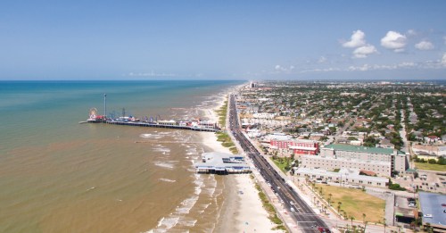 Aerial view of a coastal city with a pier, beach, and ocean, featuring colorful buildings along the shoreline.