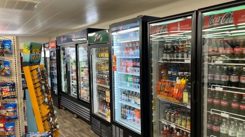 A convenience store aisle with multiple beverage coolers filled with various drinks and snacks on display.