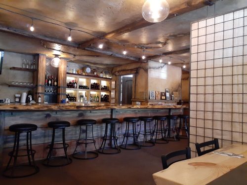A rustic bar interior with wooden shelves, stools, and soft lighting, featuring a minimalist design and a cozy atmosphere.