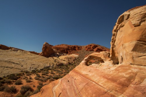 A colorful desert landscape featuring layered rock formations and a clear blue sky.