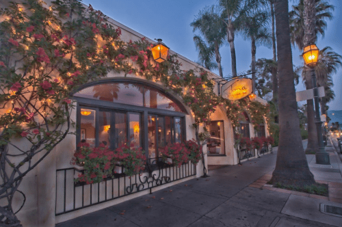 Charming restaurant exterior adorned with flowers and lanterns, surrounded by palm trees at dusk.