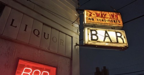 Neon signs for a bar and liquor store at night, with a vintage "2-Way Inn" sign illuminated.