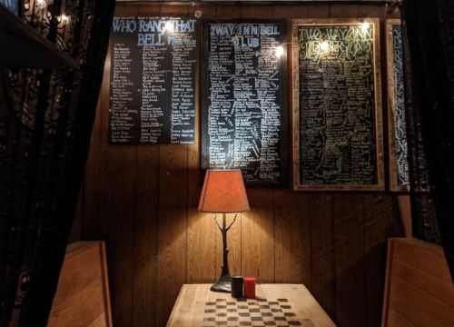 A cozy interior with wooden walls, a lamp on a table, and chalkboard menus listing names and items.
