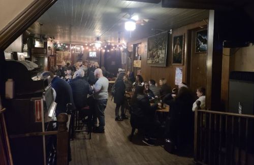 A lively bar scene with people socializing, dim lighting, and wooden decor, creating a warm atmosphere.