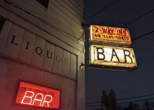 Neon signs for a bar and liquor store illuminated at night, with a vintage "2-Way Inn" sign above.