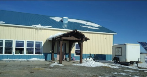 A building with a blue roof, snow on the roof, and a trailer parked outside on a clear winter day.