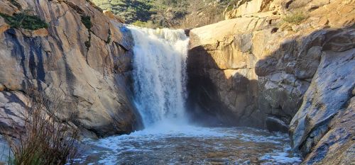 A cascading waterfall flows over rocky cliffs into a serene pool below, surrounded by lush greenery.