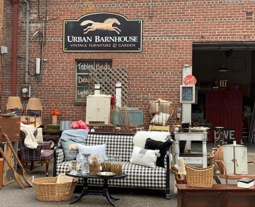 A cozy outdoor display of vintage furniture and decor at Urban Barnhouse, featuring a checkered sofa and various accessories.