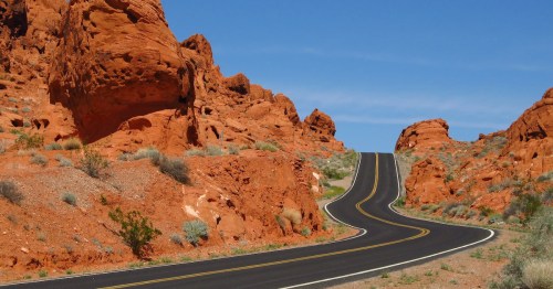 Winding road through vibrant red rock formations under a clear blue sky.