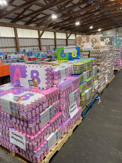 Colorful playmats and foam tiles stacked neatly in a warehouse, labeled with letters and numbers.