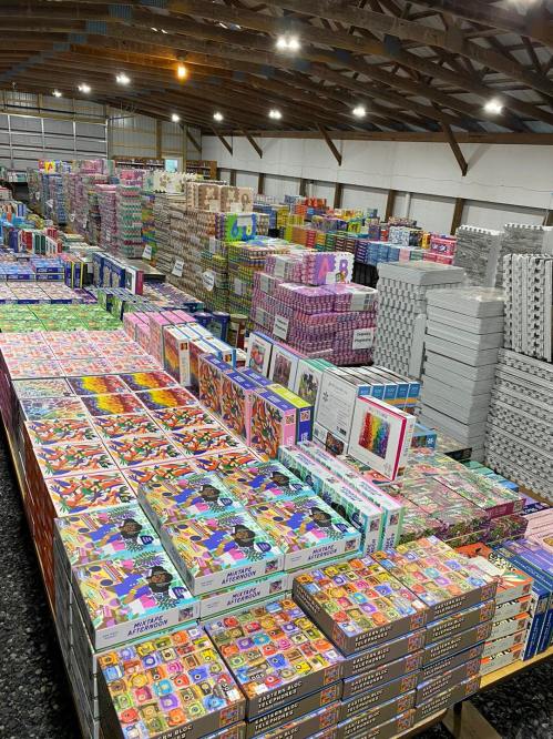 A large warehouse filled with neatly organized boxes of puzzles and games stacked on shelves and pallets.