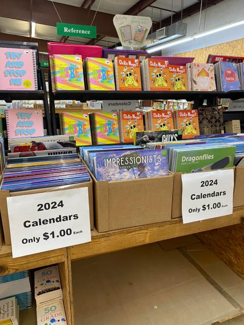 A display of 2024 calendars for sale, priced at $1.00 each, alongside various colorful books in a store.