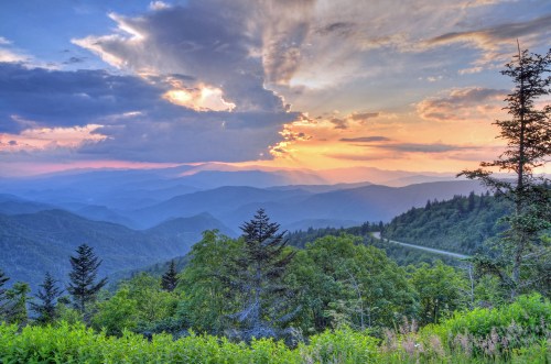 A scenic view of mountains at sunset, with vibrant clouds and lush greenery in the foreground.