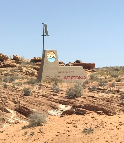 Welcome sign for Page, Arizona, set against a rocky desert landscape under a clear blue sky.