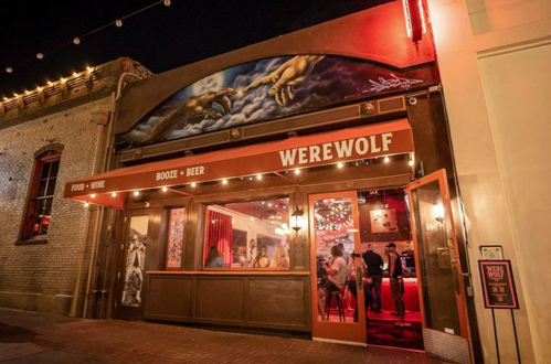 A lively bar named "Werewolf" with a vibrant entrance, featuring red lights and a mural above the door.