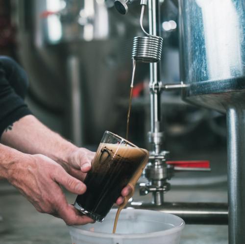 A person pours dark liquid into a glass from a metal brewing apparatus.