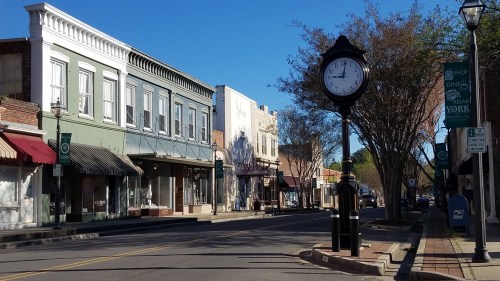 A quiet street scene featuring shops, a clock, and clear blue skies in a small town.
