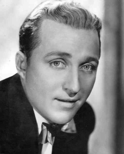 Black and white portrait of a young man in a tuxedo, smiling softly with styled hair and bright eyes.