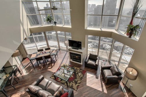 A modern, spacious living room with large windows offering a city view, featuring stylish furniture and a dining area.