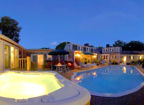 A serene evening view of a pool area with a hot tub, surrounded by cozy seating and charming buildings.