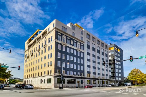 A modern multi-story building with a mix of gray and beige facades, set against a blue sky with scattered clouds.