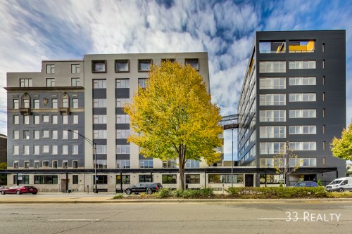 Modern multi-story buildings with large windows and autumn trees in front under a cloudy sky.