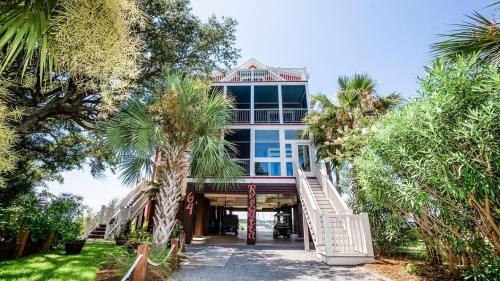 A tall beach house with multiple levels, surrounded by palm trees and greenery, featuring a welcoming entrance.