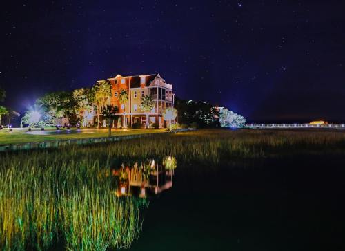 A serene night scene of a house by the water, reflecting stars and lights in the calm marsh grass.