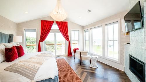 Bright, modern bedroom with a chandelier, red curtains, large windows, and stylish decor overlooking a scenic view.