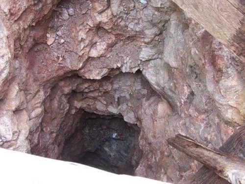 A deep, rocky mine shaft with rough, uneven walls and wooden supports at the top.