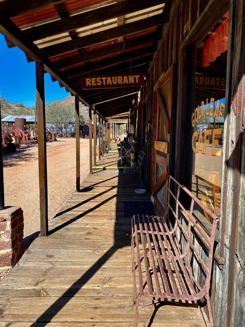 A rustic wooden walkway lined with benches, leading to a restaurant and café in a historic setting.