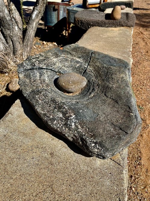 A large, flat stone with a smaller round stone resting in a depression, set on a textured surface outdoors.