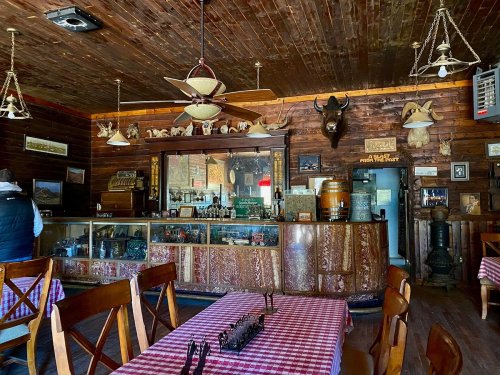 Cozy rustic bar interior with wooden decor, checkered tablecloths, and vintage items on display.