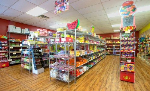 A colorful candy store interior with shelves filled with various candies and snacks, featuring bright decorations.