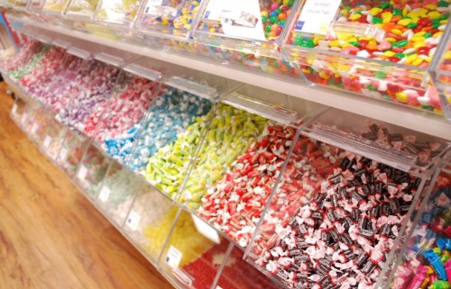 A colorful display of various candies in clear containers on a store shelf.