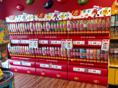 A colorful display of Jelly Belly candy dispensers filled with various flavors in a vibrant store setting.