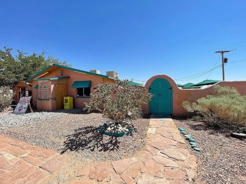 A colorful adobe-style building with a turquoise door and windows, surrounded by desert landscaping and a stone pathway.