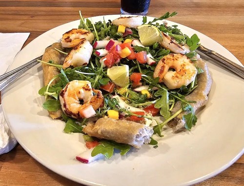 A plate of salad topped with grilled shrimp, tomatoes, lime, and greens, served on a flatbread.