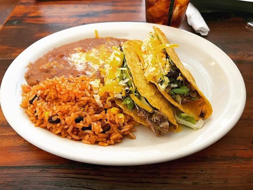 A plate with three tacos filled with meat, lettuce, and cheese, served with rice and refried beans.