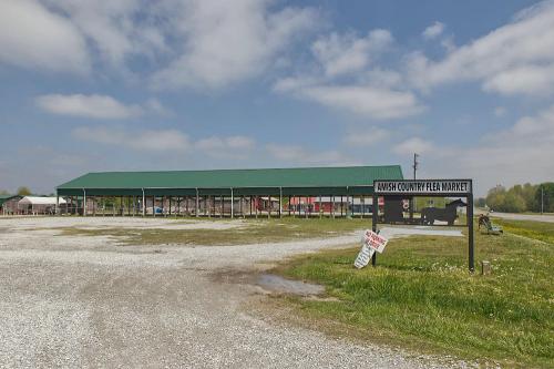 Amish Country Flea Market with a large green roof, surrounded by gravel and grass under a cloudy sky.