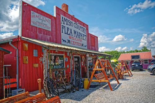 A vibrant red building with a sign reading "Amish Country Flea Market" and outdoor displays of wooden furniture and decor.