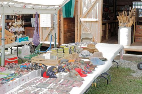A market stall displays various hats and sunglasses under a tent, with wooden items visible in the background.