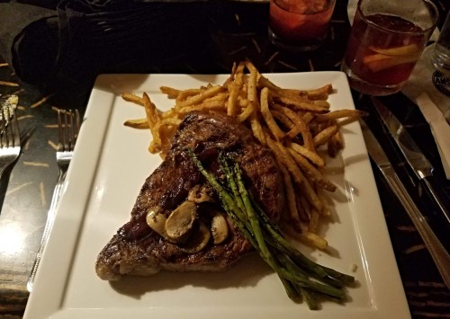 A plate featuring a grilled steak topped with mushrooms, served with French fries and asparagus.
