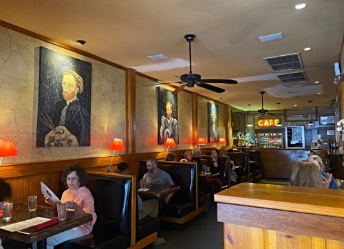 A cozy café interior with wooden accents, featuring art on the walls and patrons seated in booths.