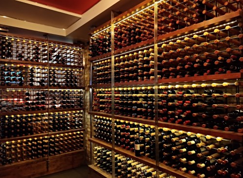 A well-organized wine cellar with wooden racks filled with numerous bottles, illuminated by warm lighting.